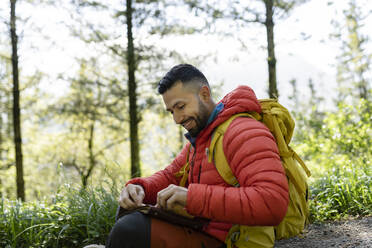 Glücklicher Mann mit Rucksack sitzt mit Tagebuch im Wald - JCCMF06285