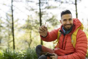 Lächelnder Wanderer mit Papierflieger im Wald sitzend - JCCMF06286