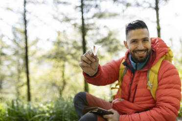 Smiling hiker with paper airplane sitting in forest - JCCMF06286