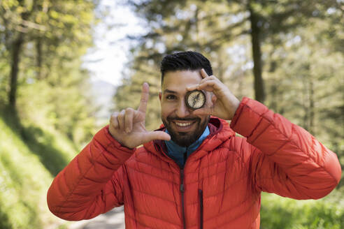 Happy man covering eye with navigational compass - JCCMF06291