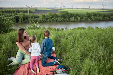 Mutter mit Tochter und Sohn betrachten am Wochenende Windkraftanlagen auf einem Feld - ZEDF04547