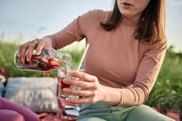 Young woman pouring infused water in glass at field on weekend - ZEDF04562