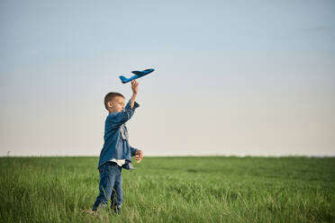 Boy throwing airplane toy in field on weekend - ZEDF04571