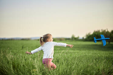 Playful girl throwing airplane in agricultural field - ZEDF04575