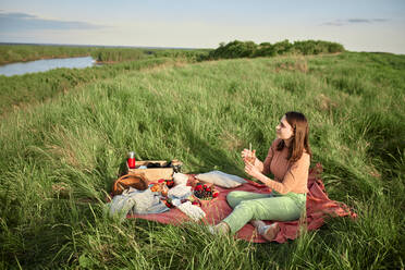 Young woman having infused water and looking at river in field - ZEDF04579