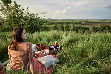Nachdenkliche Frau sitzt auf einer Picknickdecke im Feld am Wochenende - ZEDF04581