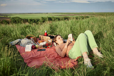 Lächelnde Frau, die beim Picknick auf einem Feld ein Buch liest - ZEDF04592