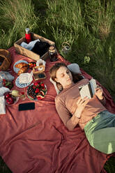 Junge Frau liest ein Buch auf einer Picknickdecke in einem Feld - ZEDF04593