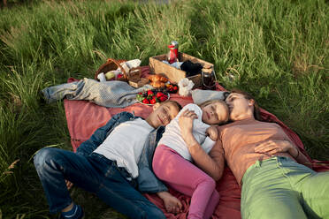 Junge Frau schläft bei Kindern auf einem Feld beim Picknick - ZEDF04595