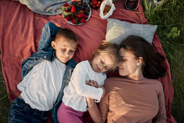 Smiling mother and children sleeping in field at picnic - ZEDF04597