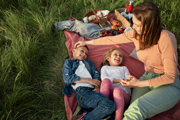 Mother sitting by happy children on picnic blanket - ZEDF04602