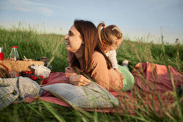 Smiling young woman lying on front by daughter in agricultural field - ZEDF04603