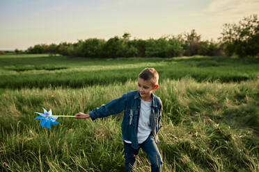 Junge mit Windradspielzeug läuft auf Gras auf einem Feld - ZEDF04608