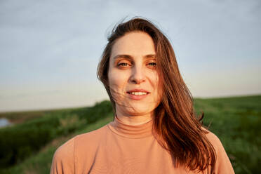 Smiling young woman with brown hair in field at sunset - ZEDF04618