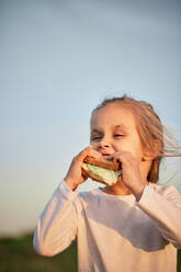 Girl eating sandwich in front of sunset sky - ZEDF04619