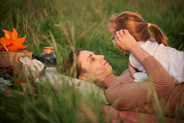 Mother talking with daughter lying on grass - ZEDF04620