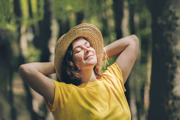 Contemplative woman with hands behind head relaxing in forest - OMIF00810