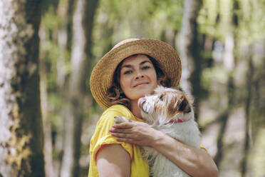 Woman carrying dog in forest - OMIF00811