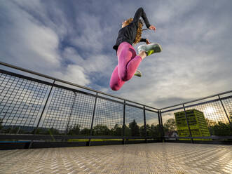 Young woman jumping in sports park at sunset - STSF03216