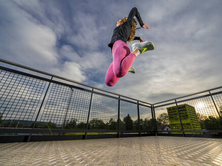 Junge Frau springt bei Sonnenuntergang im Sportpark - STSF03216