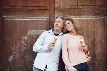 Contemplative couple having ice cream in front of door - JOSEF09599