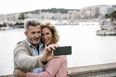 Lächelnde Frau umarmt Mann nimmt Selfie vor dem Meer - JOSEF09602