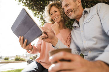 Happy mature couple using tablet computer in park - JOSEF09603