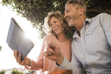 Cheerful mature couple using tablet PC in park - JOSEF09604