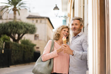 Cheerful woman looking at man with ice cream on street - JOSEF09608