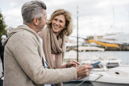 Lächelnde Frau im Gespräch mit einem Mann mit Tablet-PC am Hafen - JOSEF09636