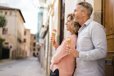 Thoughtful mature couple with ice cream standing in alley - JOSEF09663
