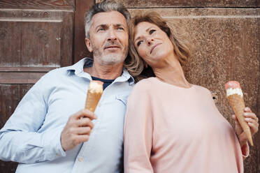 Contemplative mature couple with ice cream in front of door - JOSEF09664