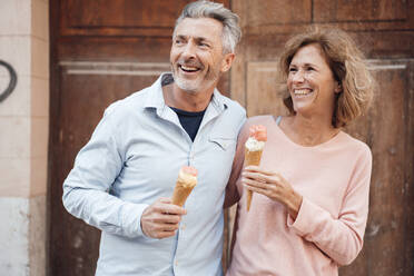 Cheerful mature couple with ice cream in front of door - JOSEF09665