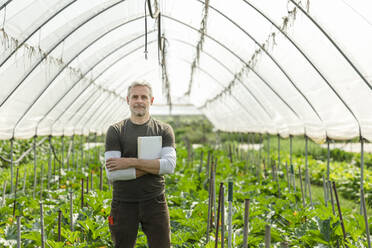 Confident farmer with tablet PC standing in greenhouse - MCVF00968