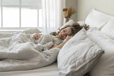 Smiling young woman sleeping in bed at home - VPIF06039