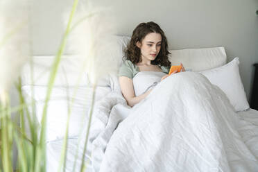 Schöne Frau mit Smartphone sitzt auf dem Bett zu Hause - VPIF06040
