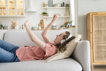 Happy woman wearing wireless headphones enjoying music at home - VPIF06053