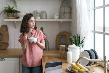 Woman eating breakfast by kitchen counter at home - VPIF06056