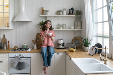 Woman with bowl sitting on kitchen counter at home - VPIF06057