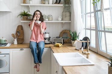 Woman eating breakfast sitting on kitchen counter at home - VPIF06059