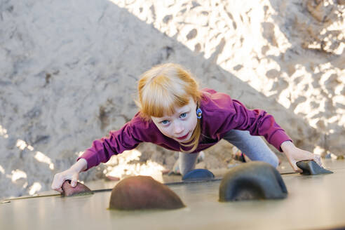 Mädchen mit roten Haaren klettert auf dem Spielplatz an der Wand - IHF00792