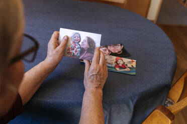 Einsame ältere Frau hält ein Familienfoto am Tisch - IHF00795
