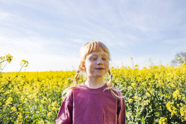 Smiling redheaded girl with eyes closed standing on rapeseed field - IHF00796