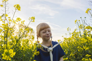 Glückliches Mädchen mit Windradmodell inmitten von Pflanzen auf einem Rapsfeld - IHF00804
