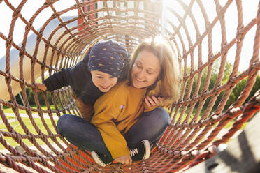 Glückliche Mutter mit ihrem Sohn, der im Klettergerüst auf dem Spielplatz spielt - IHF00810