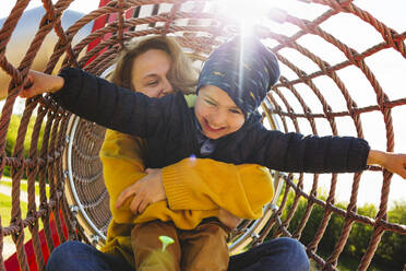 Happy boy with mother playing in jungle gym at playground - IHF00811