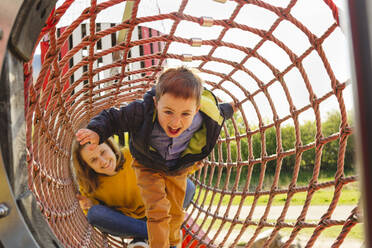 Lächelnde Frau mit Sohn im Klettergerüst auf dem Spielplatz - IHF00813