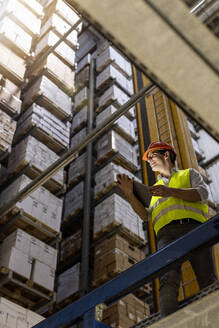 Smiling worker with tablet PC standing by railing in warehouse - PESF03796