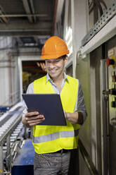 Smiling worker wearing hardhat using tablet PC in warehouse - PESF03808