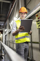 Arbeiter in reflektierender Kleidung mit Tablet-PC an einem Geländer in einem Lagerhaus - PESF03809